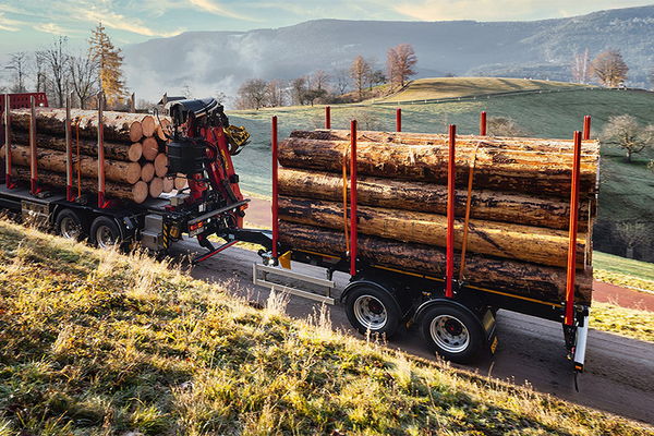 Un camion avec une remorque à essieu central de DOLL roule à l'aube sur une route de campagne étroite entre des prés et des champs