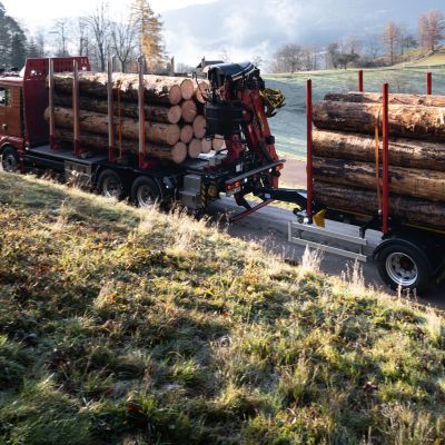 Un camion avec une remorque à essieu central de DOLL roule à l'aube sur une route de campagne étroite entre des prés et des champs