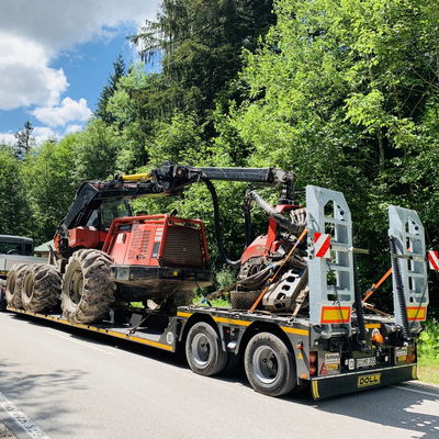 Tracteur lourd sécurisé sur une remorque plate pour transport sur une route forestière sous un ciel ensoleillé.